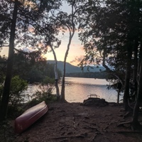 A campsite by a river at sunset with a canoe.