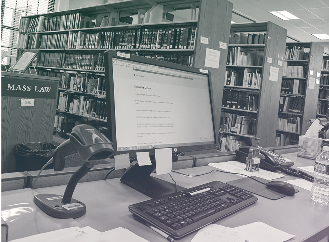 A computer in a Massachusetts Law library surrounded by bookcases and papers, with Mass.gov loaded on the screen.